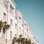 Bright modern building facade with palm trees against a clear blue sky.